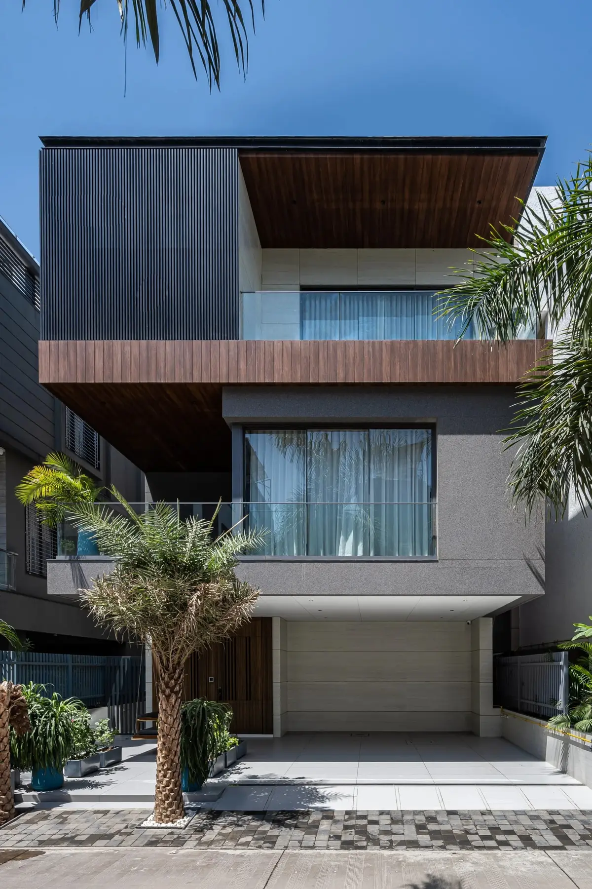 Front elevation of Maa Bungalow with dark cladding, cantilevered balconies and palm trees